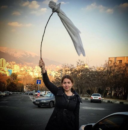 A young Iranian woman waves a white headscarf 